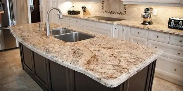 Gold and cream granite island countertop with an undermount stainless sink over dark wood cabinets