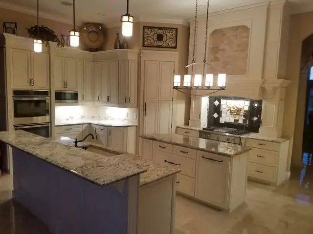 Cream raised-panel kitchen with granite tops, a dark painted island and pendant lights